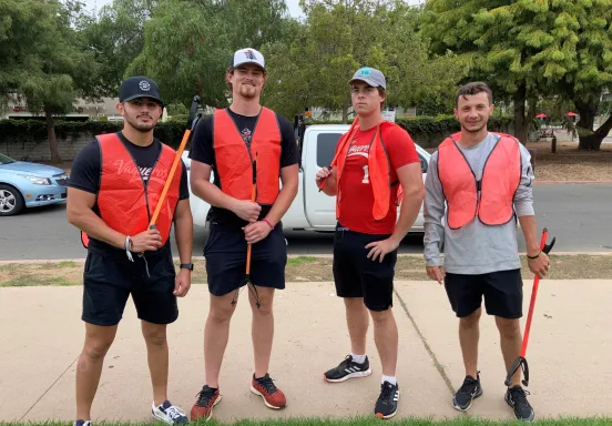 Four volunteers in orange vests participate in a community cleanup event.