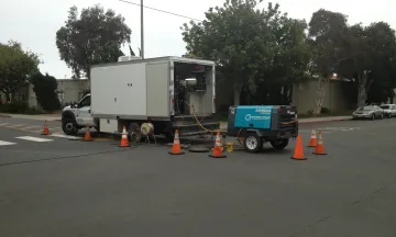 Wastewater Collection truck feeding a pipe into a drain hole.