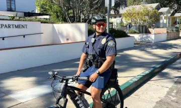 Police Department Rolls out E-Bikes to Their Fleet, image shows officer in front of Police Station on e-bike