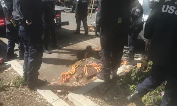 Man rescued from confined space in the Santa Barbara Harbor, image shows a man emerging from a storm drain and fire personnel surrounding him