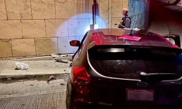 Photo from the scene showing a sedan collided with a retaining wall and an officer investigating