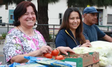 Three people smiling and handing out food.