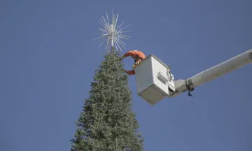 A man on a crane putting a star at the top of the holiday tree