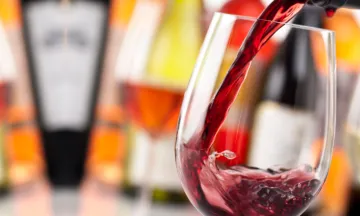 Red wine being poured into a wine glass with wine bottles in the background