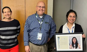 Teanna Herrera holding her recognition plaque, standing next to Chris (Airport Director) and Sara (Development Manager)