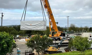 Image shows a crane lifting a large Tesla battery into the air at the Cater Water Treatment Plant