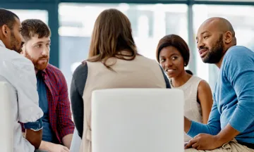 A diverse group of people sit around a table at a meeting