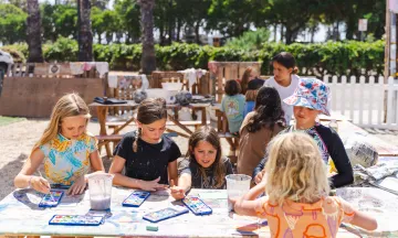 A group of campers work with water colors at an outdoor picnic table