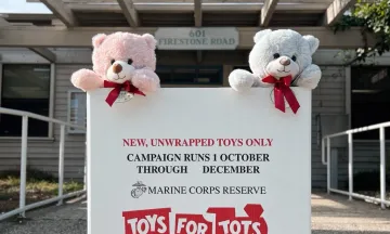 A Toys for Tots box sits in front of the Airport administration office with two teddy bears sitting on top