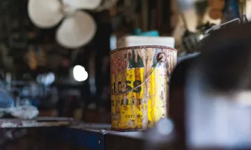 An old paint can on a shelf in a garage.
