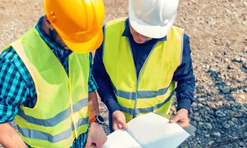 Two people in construction hats and gear reading a blueprint