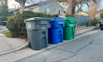 Gray (trash), blue (recycling), and green (yard waste) carts lined up on a street in Santa Barbara