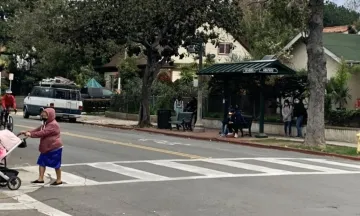 San Andres Street and Anapamu Intersection with people waiting at the bus stop, cyclist in the street and pedestrian in the crosswalk pushing a stroller.