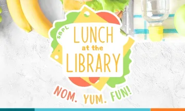 A colorful sandwich sits on a lunch table, with the text "Lunch at the Library" located on the bread and "Nom. Yum. Fun!" below.