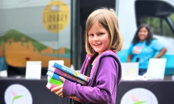 Child smiling while holding books from the Library on the Go Van.