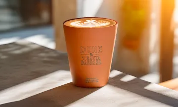 Clay cup on wood table. The cup is labeled “Dune Coffee Roasters – City of Santa Barbara.”