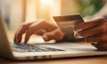 A person holding a credit card in one hand while typing with the other hand on a laptop computer