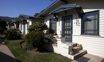 Row of small bungalows with white siding and dark trim.