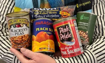 A person in a striped sweater holds assorted canned and packaged food items.