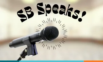 A microphone on a stand in the foreground with the text “SB Speaks!” above on a transparent room background.