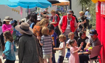 Children and adults gathered for the Children’s Resource Fair with colorful umbrellas and booths on a sunny day.)