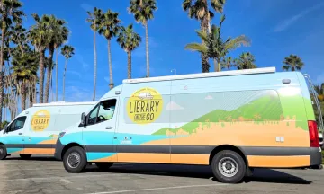 Library on the Go vans parked under tall palm trees on a sunny day with clear blue skies.
