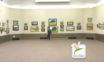 This image shows the Faulkner gallery at the Library, a patron is walking across the room looking at various art pieces