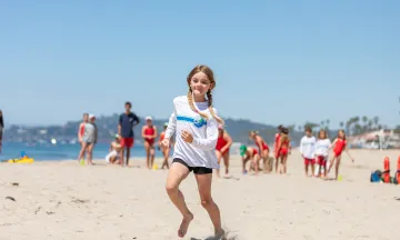 girl in white tshirt and black shorts running in the sand on the beach