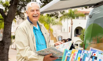Man browsing books with palm trees and historic buildings in the background