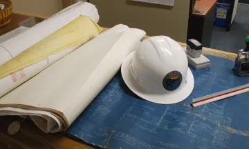 hard hat in a set of plans with a stamp and ruler also in view