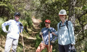 Volunteers on a trail smile while holding tools