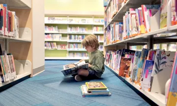 child reads a book in a library aisle