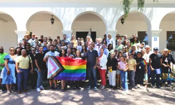 Community members gathered together holding Pride Flags on the steps of City Hall.