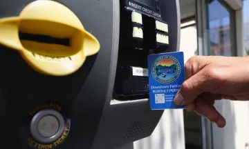 Hand holding a blue Downtown Parking monthly permit card next to a parking payment kiosk.