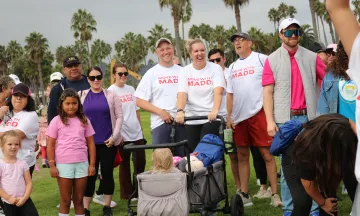 People gathered outdoors on grass, some wearing white 'MADD' shirts, smiling.