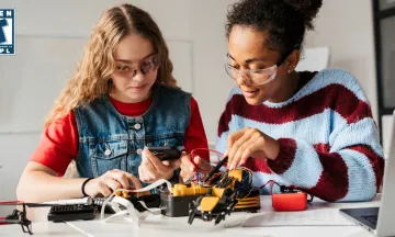 Two teenagers collaborate on assembling a STEM project, focusing on wiring and electronic components.
