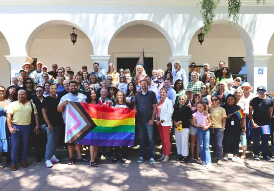 Community members gathered together holding Pride Flags on the steps of City Hall.