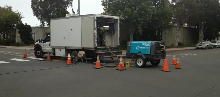 Wastewater Collection truck feeding a pipe into a drain hole. 