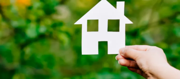 This image is a universal housing image showing a person holding a cutout of a typical house against a green grass backbround