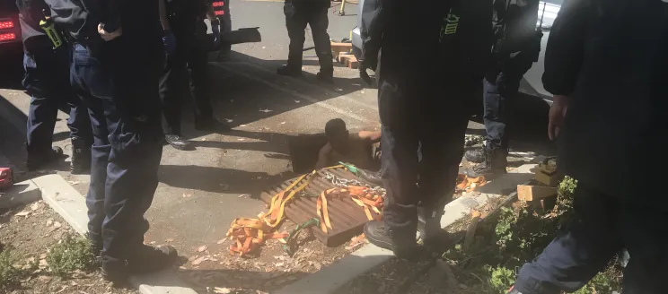 Man rescued from confined space in the Santa Barbara Harbor, image shows a man emerging from a storm drain and fire personnel surrounding him