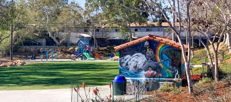Photo of a Santa Barbara park, including grass, a walkway, playground equipment and a mural of an alien on the side of a shed