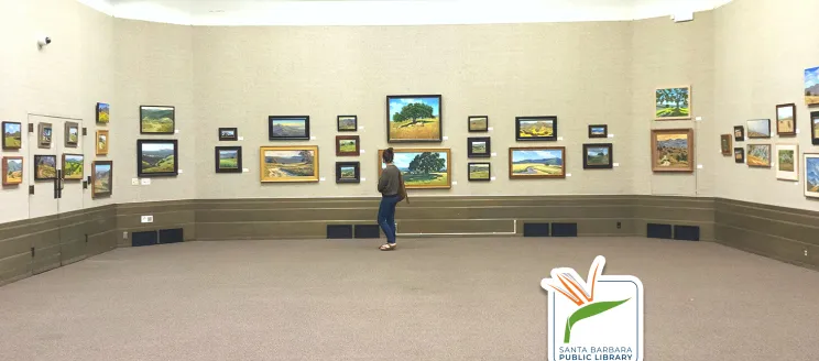 This image shows the Faulkner gallery at the Library, a patron is walking across the room looking at various art pieces