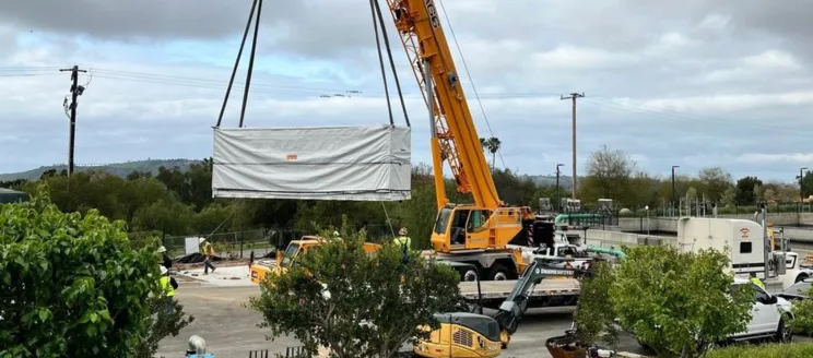 Image shows a crane lifting a large Tesla battery into the air at the Cater Water Treatment Plant