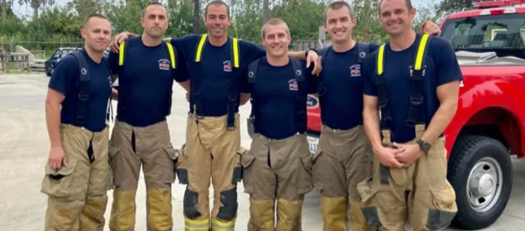 Image shows six firefighters in gear, smiling for a photo