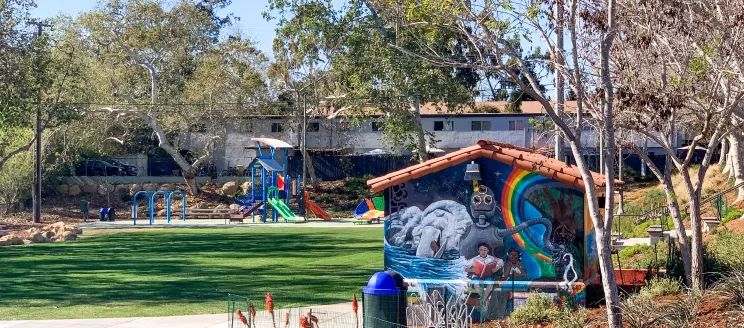 a park with a children's playground in the background and a building with a mural in the foreground