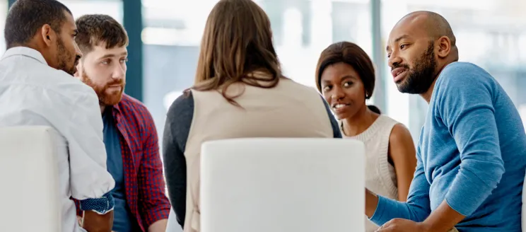 A diverse group of people sit around a table at a meeting