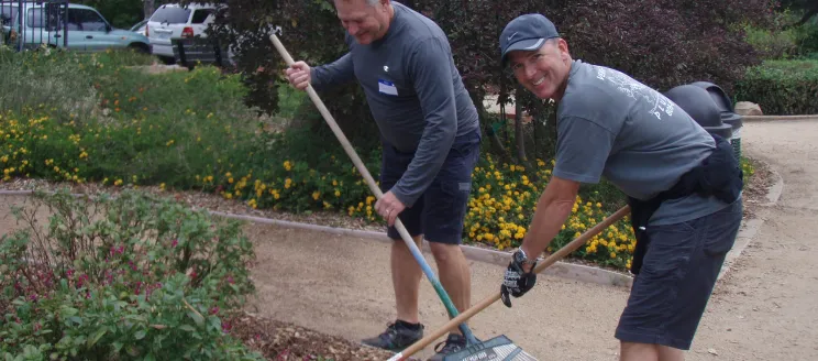 Two volunteers raking leaves and smiling in Alice Keck Park Memorial Garden
