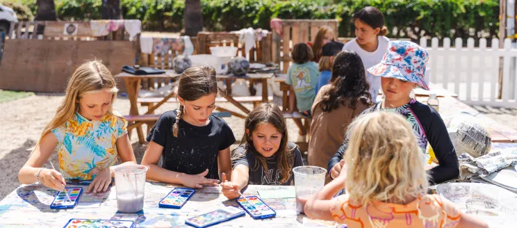 A group of campers work with water colors at an outdoor picnic table