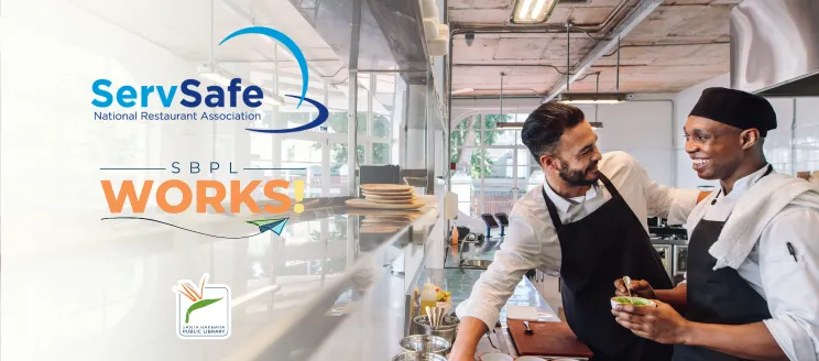 Two men in cook uniforms talk and smile in a kitchen 