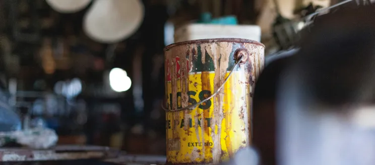 An old paint can on a shelf in a garage.